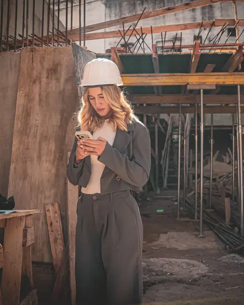 Engenheira de capacete olhando o celular dentro de uma obra