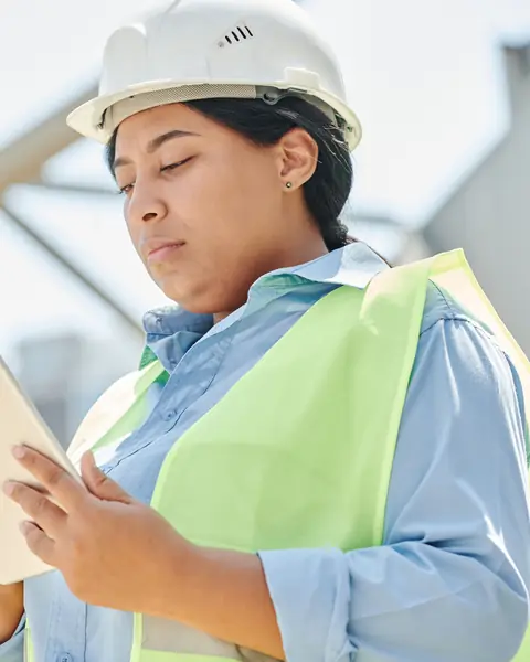 Engenheira de capacete consultando um tablet no canteiro