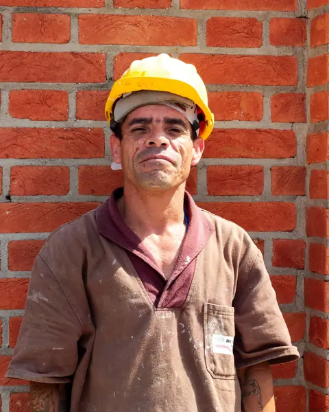 Trabalhador de capacete amarelo diante de uma parede de tijolos